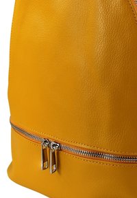 Gele leren rugzak met een gladde textuur, ronde vorm en een zilveren rits met twee trekbandjes langs de onderkant.