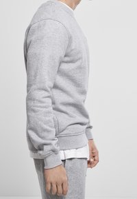 Sudadera gris de cuello redondo hecha de una tela suave, con puños y dobladillo acanalados, con un corte holgado y una camiseta blanca superpuesta debajo.
