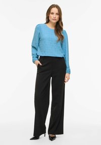 Hele sinine pikkade varrukatega pluus lillelõigetega, kombineeritud kõrge vöökohaga mustade laia säärega pükstega ja teravate mustade kontsadega.