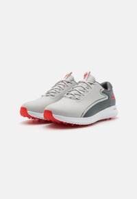Graue und weiße Sportschuhe mit roten Akzenten, ausgestattet mit einem glatten Obermaterial, einer strukturierten Zunge und einer Gummisohle mit kleinen Nocken für Traktion.