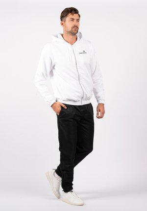Vit zip hoodie med elastiska muddar och midjeband, i kombination med svarta byxor och vita sneakers. Enkel, ren design med fokus på komfort.