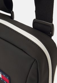 Zwarte synthetische schoudertas met witte rits en riem. Bevat een logopatch in rood, wit en blauw. Gevoerde textuur.