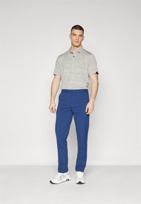 Gray striped polo shirt with short sleeves; blue trousers; white sneakers with gray accents. Model stands against a plain background.