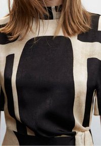 Šaty vyrobené z lehké tkaniny s béžovým pozadím a výraznými černými abstraktními tvary. Vysoký límec, krátké rukávy a stažený pas.