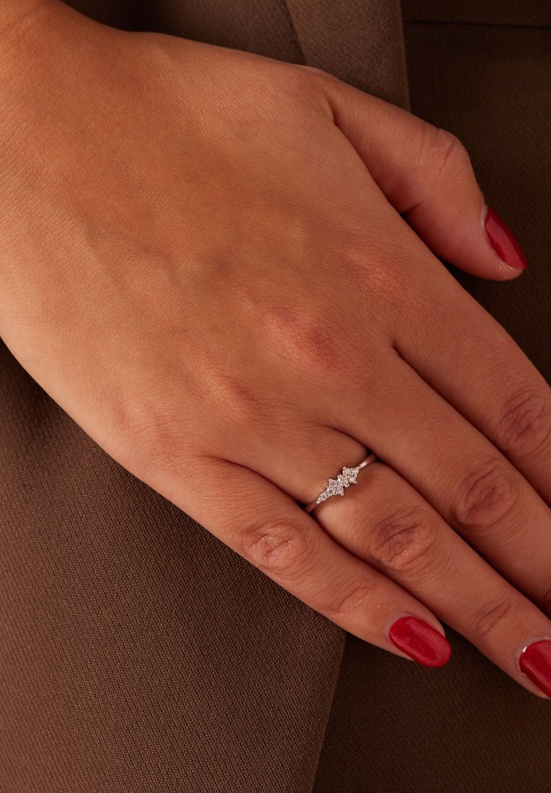 Bague en argent avec trois accents ressemblant à des diamants, montés sur un bandeau délicat. Main posée sur une surface texturée marron, mettant en valeur le bijou.