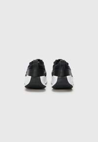 Baskets noires et blanches avec une tige en mesh texturé, un design élégant, un talon renforcé et un détail de logo au dos.