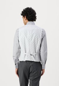 Hellgraue Weste mit geometrischem Muster, weicher Textur, verstellbarem Rückenriemen, die zu einem Hemd mit Knöpfen passt.