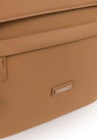 Borsa in pelle marrone chiaro con texture liscia, dotata di chiusura con zip e etichetta logo impresso. Design pulito con dettagli di cucitura sottili.