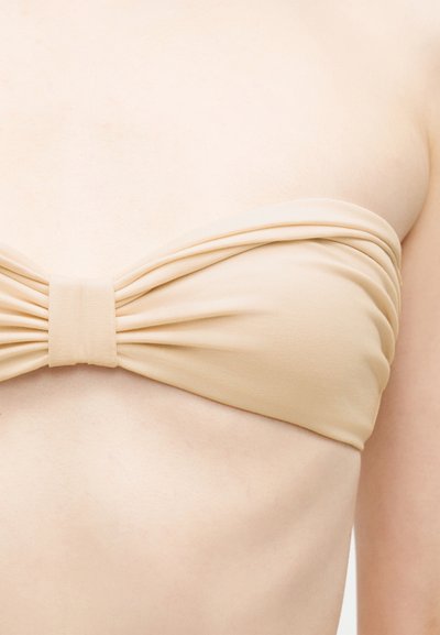 Haut bandeau beige sans bretelles avec tissu froncé et nœud central porté sur un torse à peau claire.