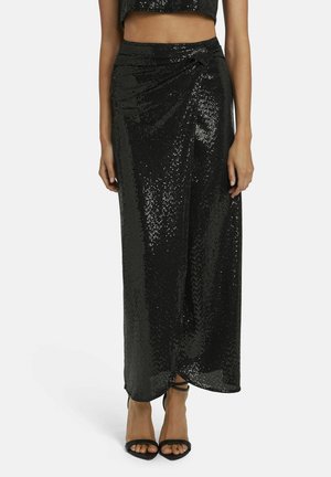 Zwarte maxi rok van pailletten met een wikkelontwerp, voorzien van een gedraaide detail bij de taille en een gladde textuur. Gecombineerd met zwarte hoge hakken.