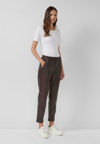 Bruine tapered broek met een elastische tailleband en zijzakken, gecombineerd met een witte t-shirt met ronde hals en witte sneakers.