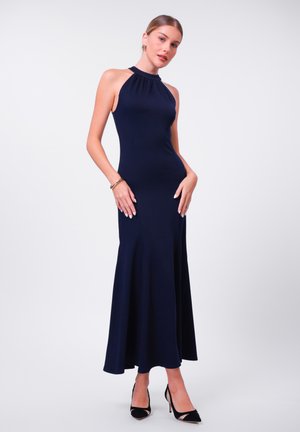 Navy halter neck dress, fitted silhouette, flared hem, seamless fabric, worn with black high-heeled shoes, minimalistic gold jewelry accents.
