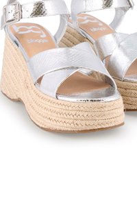 Sandalias de cuña metálicas plateadas con tiras entrelazadas, suela envuelta en yute y acabado texturizado. Acentuadas con un cierre de hebilla.
