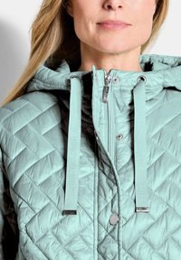 Gequilted pufferjack in mintgroen met een capuchon. Voorzien van bijpassende trekkoorden en zilveren ritsen, gedetailleerd met een metalen logo-knop.