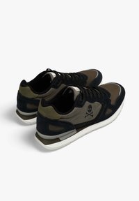 Un par de zapatillas negras y verdes oliva con suelas blancas, cordones negros y un logo de calavera y huesos cruzados en los paneles laterales.