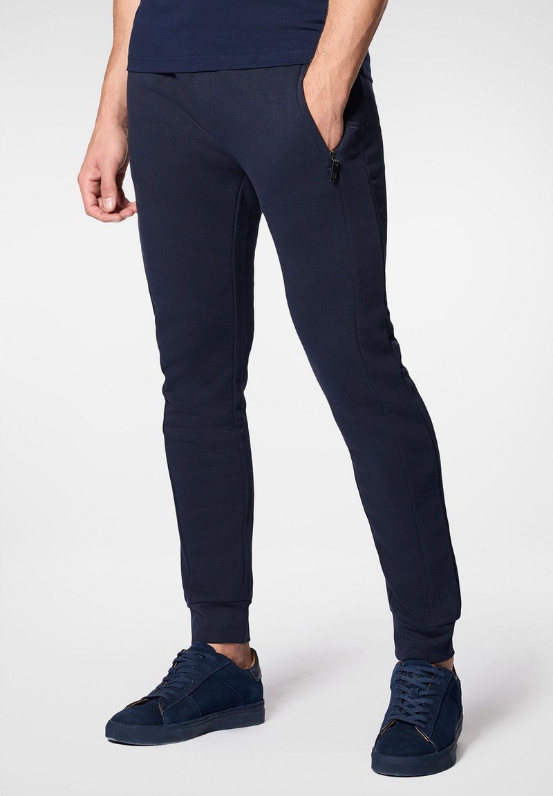 Granatowe dresy o dopasowanym kroju, z elastycznymi mankietami i bocznymi kieszeniami na zamek, wykonane z miękkiego materiału. W komplecie z pasującymi granatowymi trampkami.