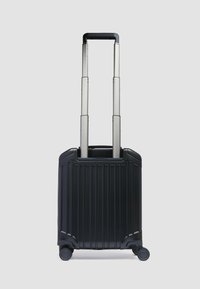 Schwarzer Hartschalenkoffer mit vertikalen Rillen, ausziehbarem silbernem Griff, vier Rädern und stabilem Boden für erhöhte Standfestigkeit.