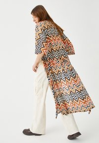 Kimono w wzór chevron w jaskrawych kolorach pomarańczowym, czarnym i kremowym; luźny krój, krótkie rękawy i swobodny tył. Noszone na lekkich spodniach.