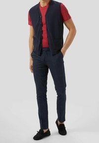 Námořnická pletená vesta, červená polokošile, kostkované námořnické kalhoty a černé mokasíny. Jednoduchý design s knoflíky a dvěma kapsami na vestě.