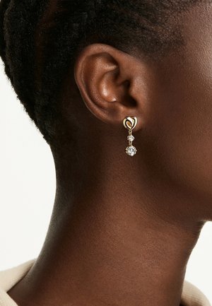 Orecchini a goccia d'oro con una spilla a forma di cuore e due cristalli trasparenti pendenti sotto. Gli orecchini sono progettati per completare vari outfit.