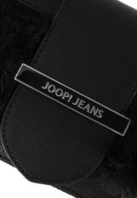 Černá taška z umělé kůže s texturovaným povrchem, s lesklou kovovou destičkou se značkou "JOOP! JEANS" a měkkými černými kožíškovými akcenty.