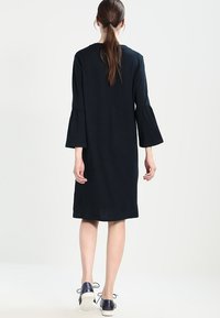 Černé šaty ke kolenům s dlouhými zvonovými rukávy, hladkou texturou, kulatým výstřihem a jemně A-čkovým střihem. V kombinaci s námořnickými botami.