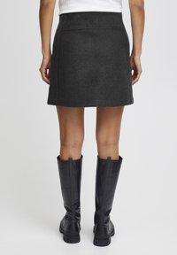 Mörkgrå ull mini kjol med åtsittande midja och lätt utsvängd form, matchad med svarta knähöga stövlar. Slät textur, rena linjer.