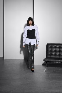 Hvid skjorte med knaplukning lagdelt med en sort korsært over skinnende, mørke, pailletbelagte flarebukser. Sorte hæle og en elegant sort sofa i baggrunden.