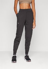 Pantalons de sport noirs avec une coupe fuselée, dotés de poches latérales, d'une taille haute et d'un petit logo blanc sur la cuisse.