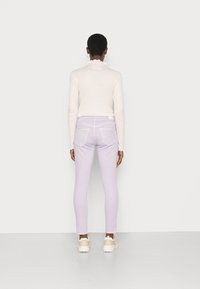 Jeans skinny lilás com uma textura suave, costuras brancas, bolsos traseiros e uma cintura alta. Combinados com uma blusa justa de mangas longas na cor creme.