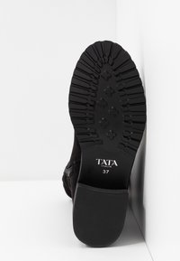 Semelle de botte noire avec un motif de crantage profond, marquage "TATA ITALIA" et taille 37 affichée sur un fond blanc en coin.
