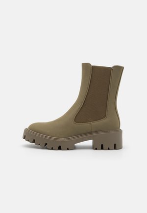 Olivengröna ankelboots med elastiska sidopaneler, kraftig gummisula, slät textur och rund tå. Minimalistisk design utan synlig hårdvara.