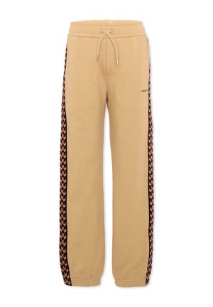 Pantalon de survêtement beige avec taille et poignets élastiques, cordon de serrage et bandes latérales à motifs noir, rouge et beige, avec un petit texte sur la cuisse gauche.