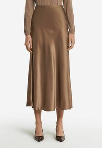 Jupe midi en satin marron avec une texture lisse, présentant un design évasé et un éclat subtil. Associée à des escarpins marron à bout pointu.