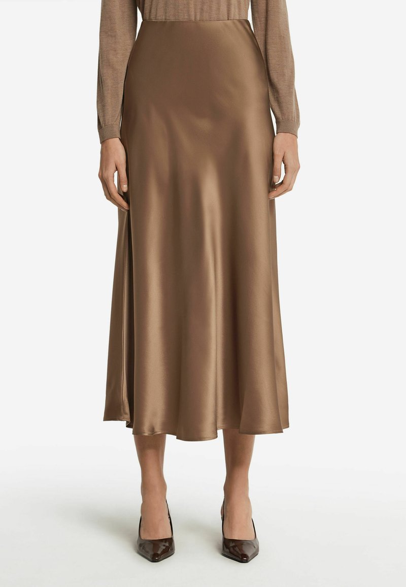 Jupe midi en satin marron avec une texture lisse, présentant un design évasé et un éclat subtil. Associée à des escarpins marron à bout pointu.
