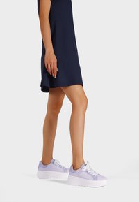 Sneaker viola chiaro con accenti sintetici bianchi, superficie testurizzata, punta rotonda, suola piatta e lacci bianchi; indossato con un vestito blu navy.