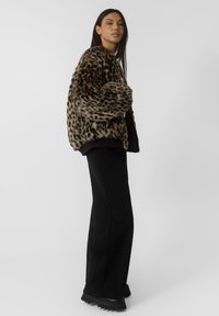 Jakna od umjetnog krzna s printsom leopard, s širokim, mekanim ovratnikom, prevelikim rukavima i opuštenim krojem, u kombinaciji s crnim širokim hlačama i čizmama.