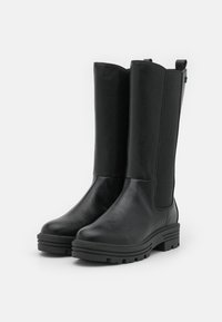 Bottes noires montantes jusqu'au genou avec une tige en cuir synthétique lisse, des panneaux latéraux élastiques et des semelles en caoutchouc robustes à relief texturé.