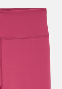 Fuksjowe legginsy z wysokim stanem, wykonane z elastycznego, gładkiego materiału z płaskimi szwami, bez widocznych wzorów i elementów metalowych.