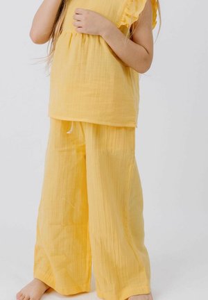 Child wearing loose yellow pants and a matching short-sleeve top, standing barefoot against a white background.