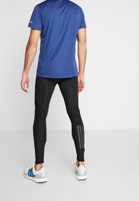 Leggings athletic neri con vestibilità affusolata, caratterizzati da motivi grigi e zip alla caviglia. Abbinati a una maglietta blu a maniche corte.