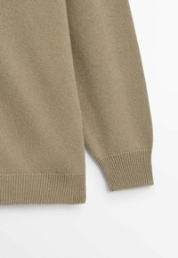 Olive green knitted sweater with a soft texture, featuring ribbed cuffs and hem. The body is slightly oversized with loose sleeves.