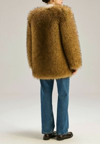 Brązowy sztuczny futerko o puszystej teksturze, oversize'owy krój i długie rękawy. Połączony z niebieskimi spódnicami dzwonami i ciemnymi loafersami.