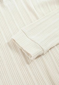 Gerippter, cremefarbener Strickpulloverstoff mit einem strukturierten Muster, umgeschlagenem Saum und Bündchen, das kleine, gleichmäßig verteilte vertikale Linien zeigt.