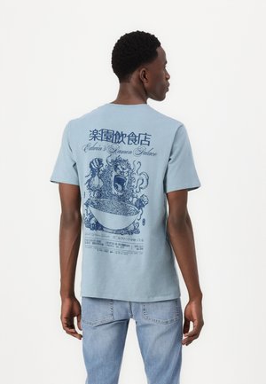 Helles blaues Baumwoll-T-Shirt mit einem grafischen Motiv einer Schüssel Ramen, einem Wesen und Text auf der Rückseite in dunkler blauer Tinte. Kurzarm.