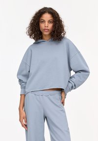 Haut à capuche court bleu clair avec une poche avant, un cordon de serrage au niveau de la capuche et des manches larges, associé à un pantalon ample assorti. Tissu doux et texturé.