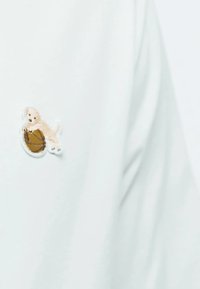 Lys blå stof med et lille broderet design af en beige hund, der leger med en brun basketball, med hvide kantdetaljer.