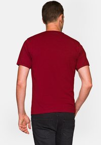 Bordowy t-shirt z krótkim rękawem z okrągłym dekoltem, wykonany z bawełnianego materiału, o gładkiej strukturze i regularnym kroju, noszony przez osobę widoczną z tyłu.