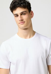 Vitt crewneck-t-shirt i mjuk bomull. Korta ärmar, slät textur och en standardpassform, lämplig för avslappnad vardagsklädsel.