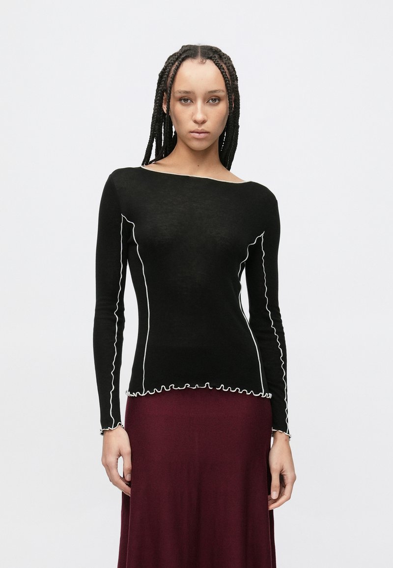 Czarna bluzka z długim rękawem, białym zygzakowatym przeszyciem wzdłuż dekoltu i dołu, zestawiona z bordową spódnicą. Gładka faktura.